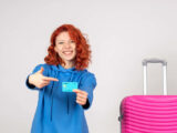 Mulher turista segurando um cartão ao lado de uma mala rosa